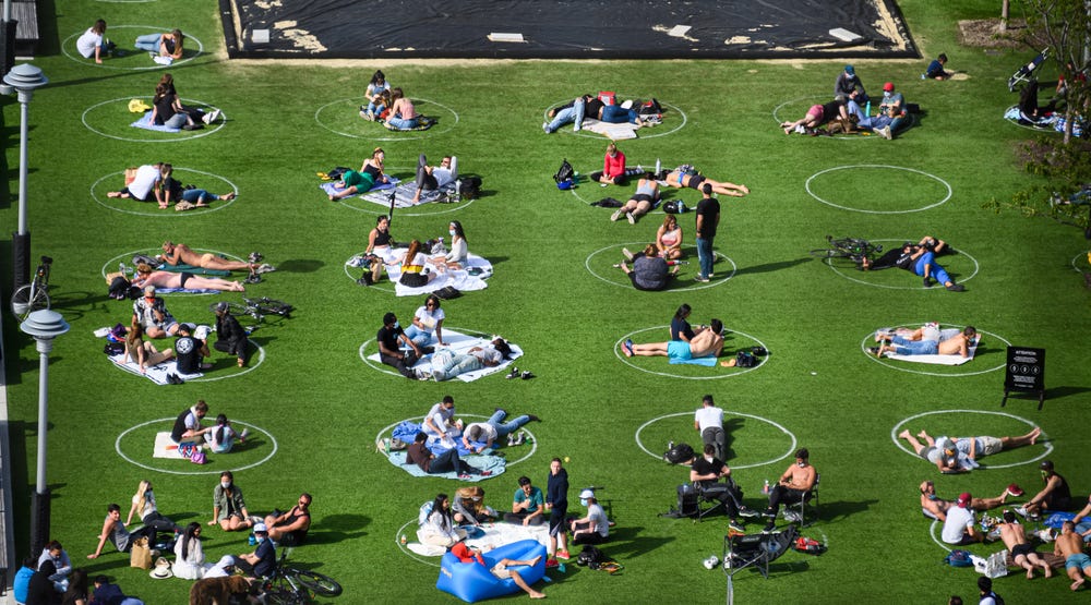 Photo of an outdoor lawn space in New York with white circles drawn on the ground and people relaxing within them.